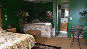 A bedroom with a bed, a small table, a chair, a bathroom, and a green wall. - Branford Motel (Branford)