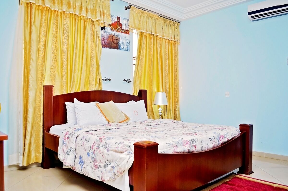 Un dormitorio con una cama de madera, cortinas amarillas, una lámpara blanca y un aire acondicionado instalado en la pared.