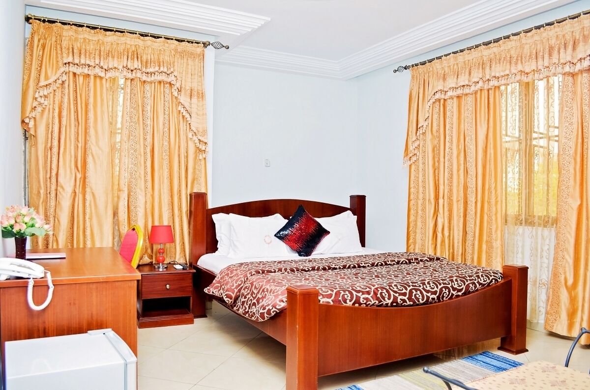 Una habitación de hotel con una cama de madera, un escritorio con teléfono, una silla y cortinas.