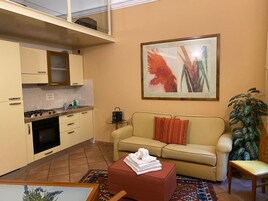 Un ambiente compatto con angolo cottura, divano, tavolino e un grande quadro astratto.
