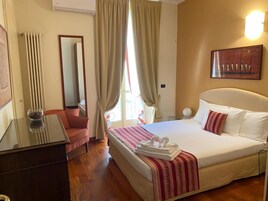 A hotel room with a bed, a desk, a chair, a mirror, and a window with curtains.