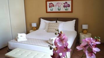 Camera d'albergo con un letto grande, due comodini con lampade, una panca ai piedi del letto e un quadro di fiori appeso al muro.