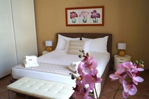 Habitación de hotel con una cama grande, dos mesitas de noche con lámparas, un banco al pie de la cama y un cuadro de flores colgado en la pared.