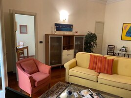 Un soggiorno con un divano giallo, una poltrona rossa, un tavolino in vetro e una libreria.