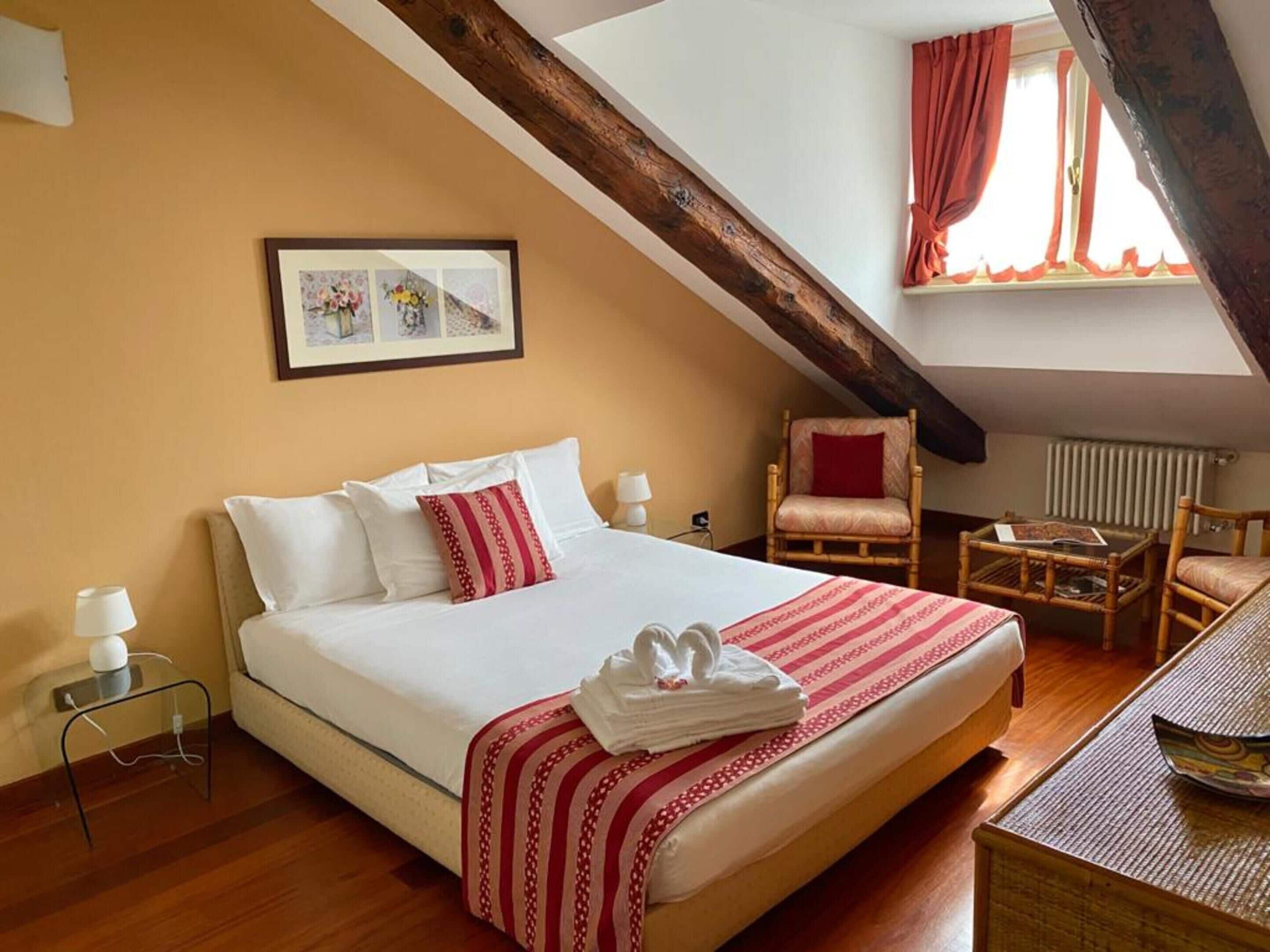 Una habitación de hotel con una cama grande, una silla, una mesita y un cuadro en la pared.