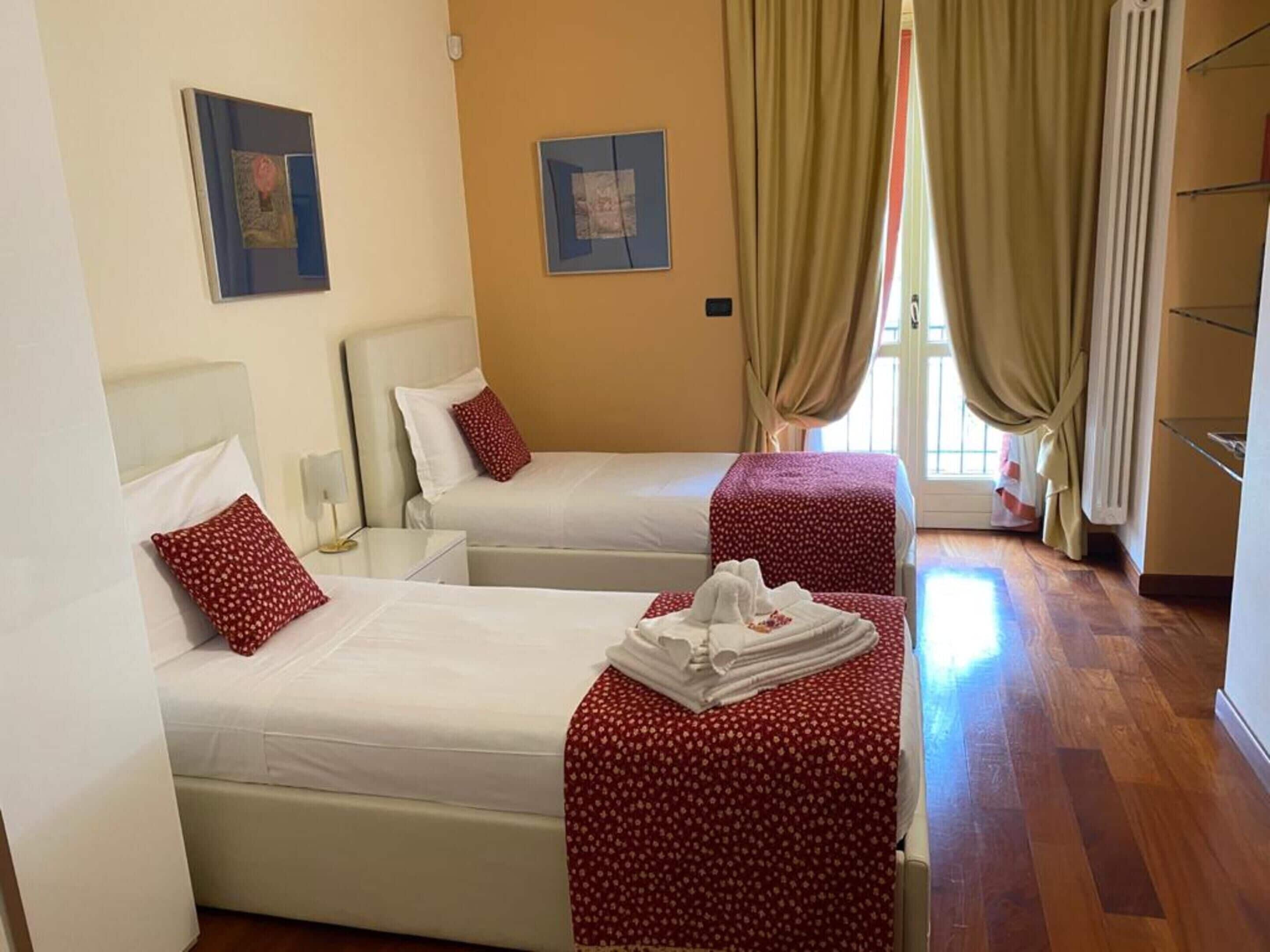 A hotel room with two beds, a small table, and a window with curtains.