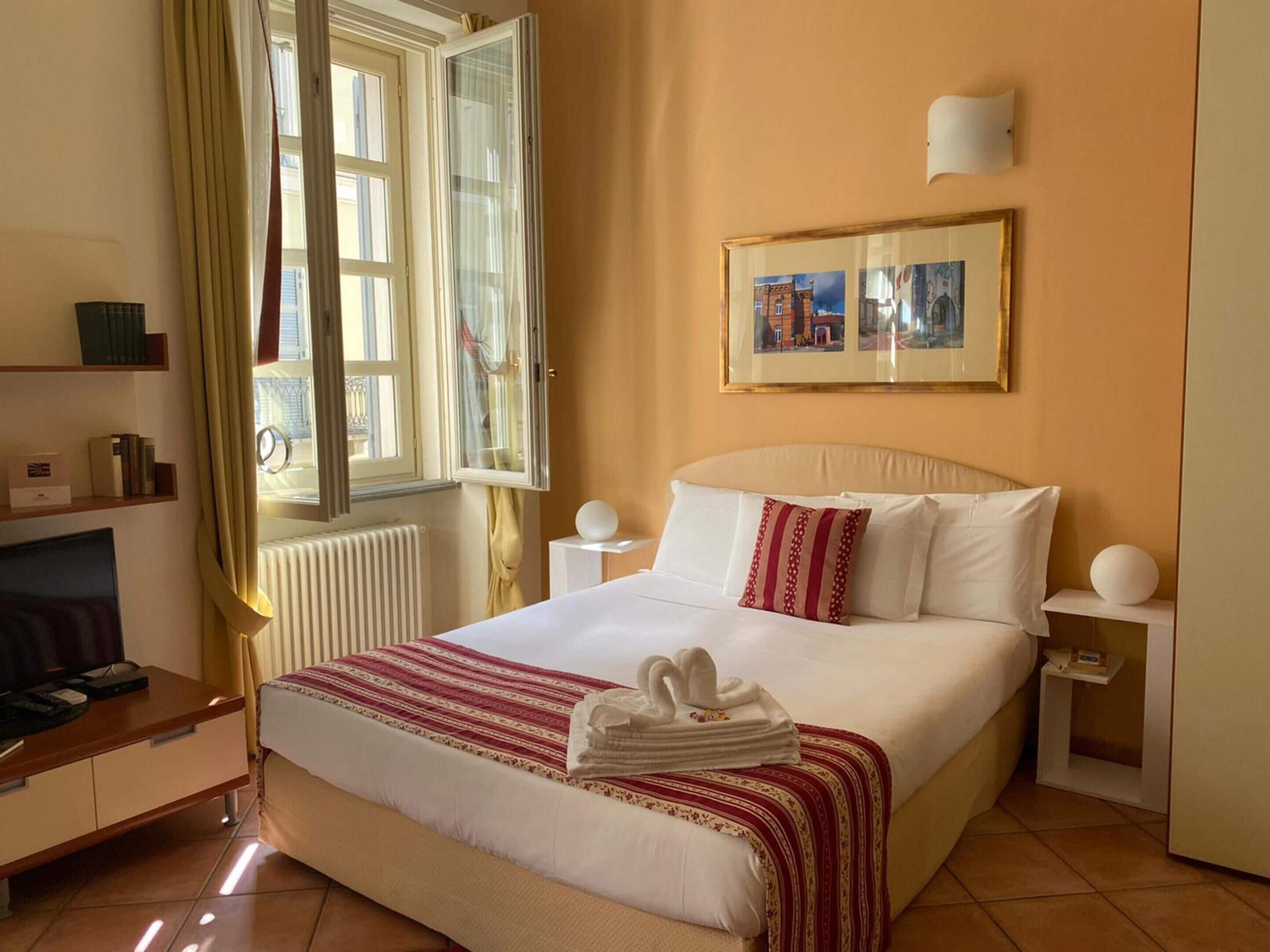 A hotel room with a large bed, a TV, a desk, and a window with curtains.