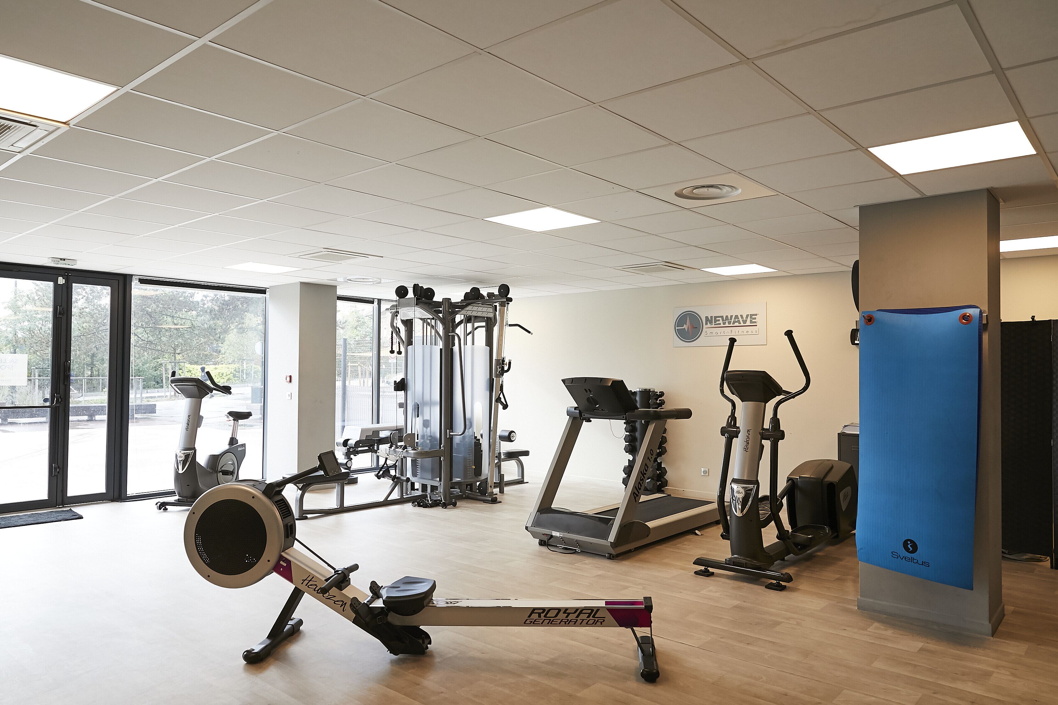 Een fitnessruimte met diverse trainingsapparaten, waaronder een roeimachine, elliptische trainer en loopbanden.