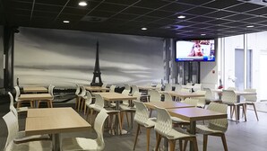 Ein Restaurant mit Tischen und Stühlen, einem großen Bildschirm, der eine Nachrichtensendung zeigt, und einem Hintergrundbild des Eiffelturms.