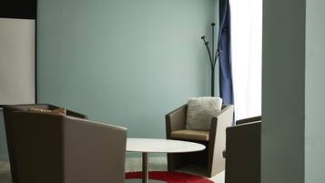A room with a round table, two chairs, a red rug, and a blue curtain.