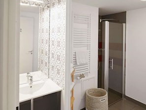 A bathroom with a white sink, mirror, towel rack, shower, and a wicker basket.