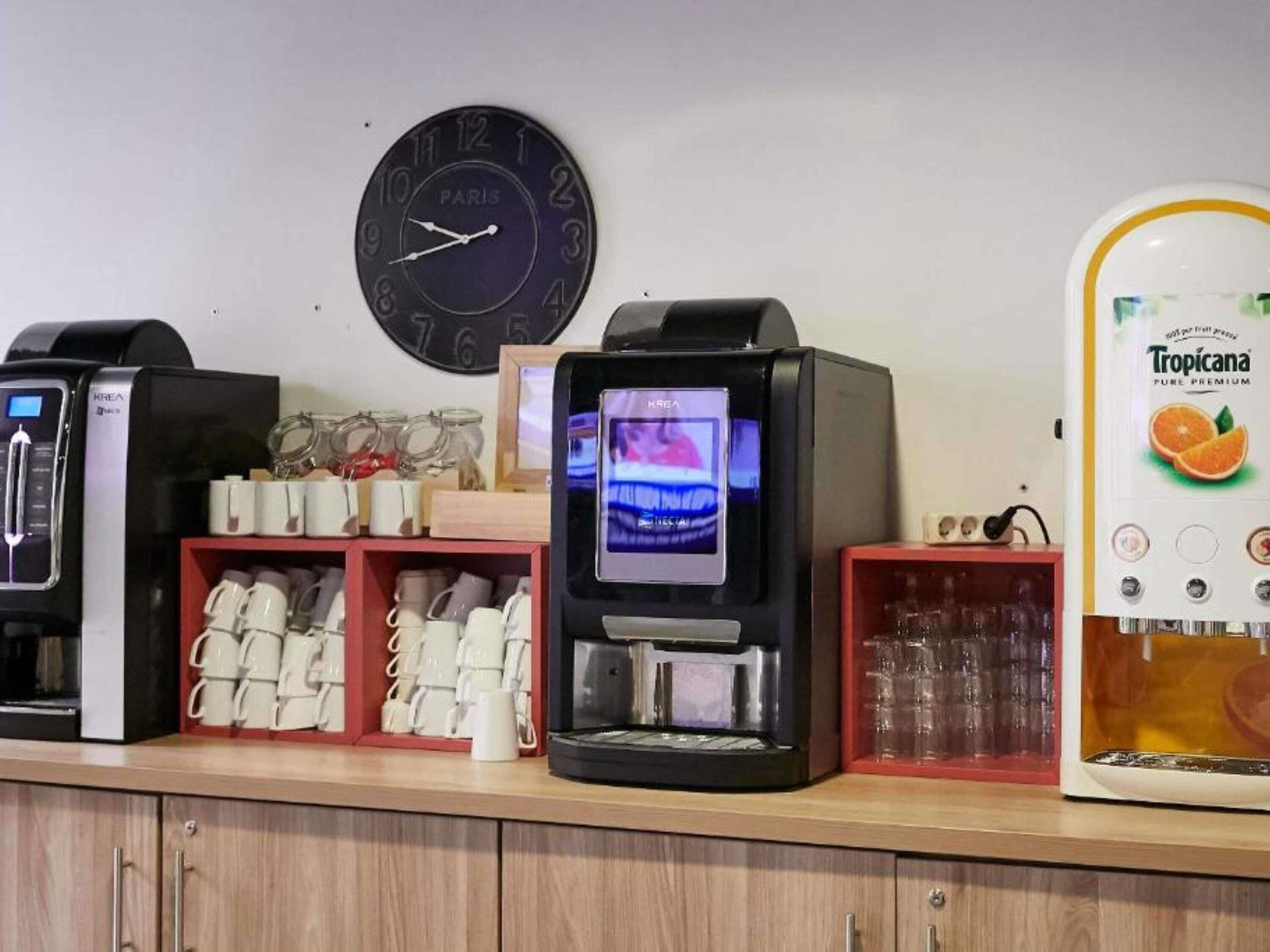 Estação de café com várias máquinas de café, um relógio e uma geladeira.
