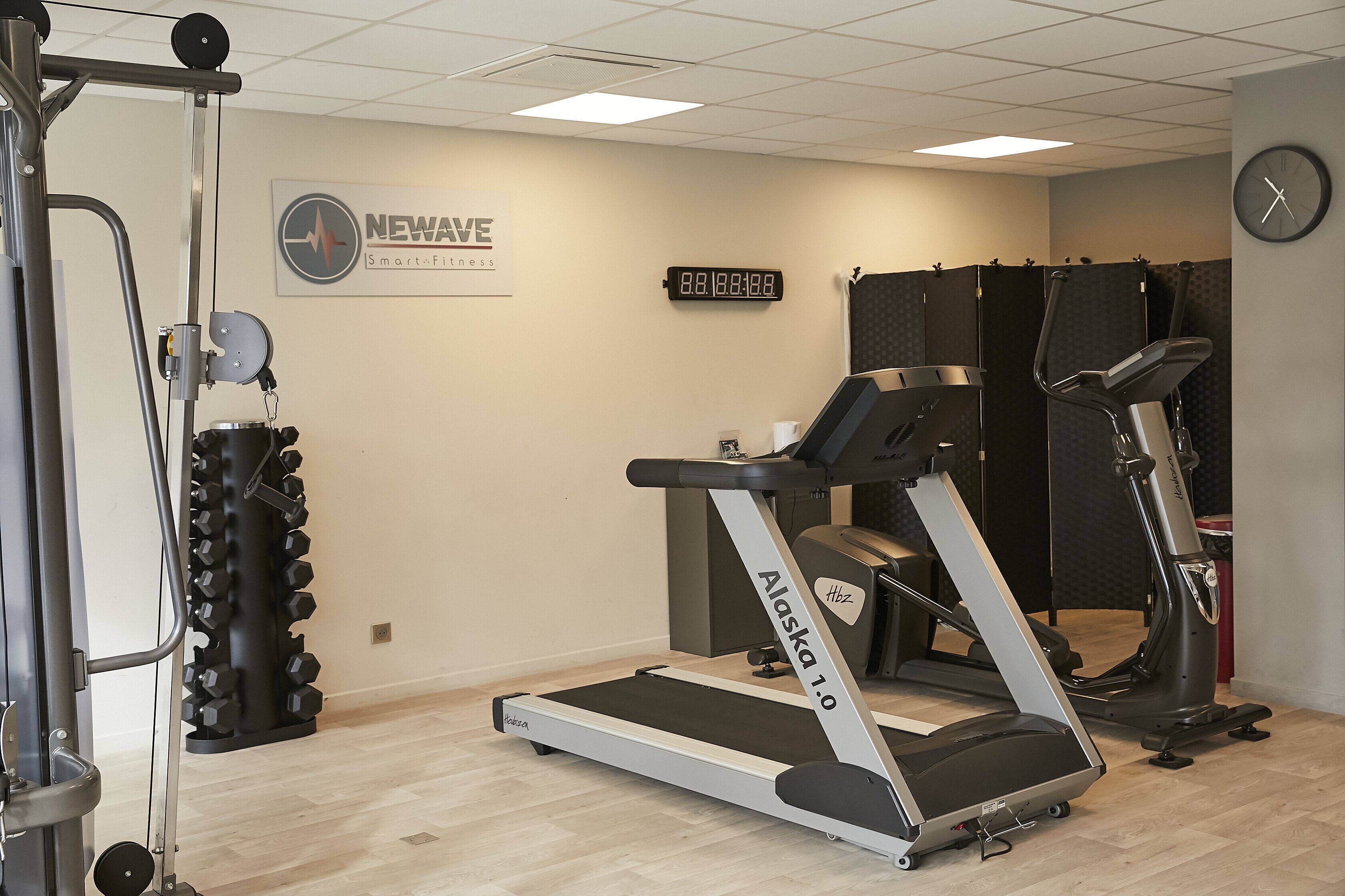 Een fitnessruimte met een loopband, krachtapparaat en gewichten.