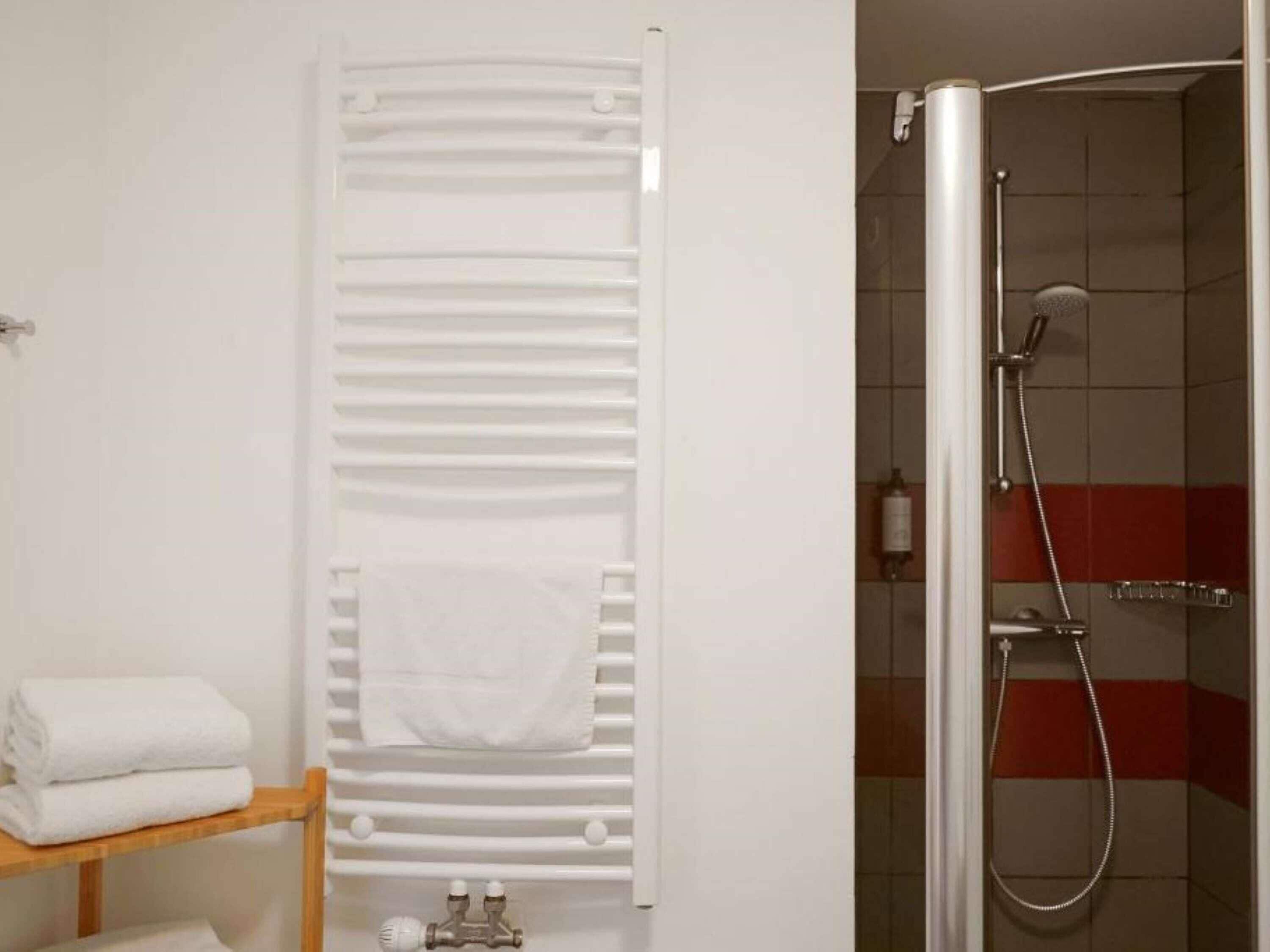 A bathroom with a towel rack, a shower, and a shelf with folded towels.