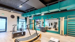 Ein Fitnessraum mit Trainingsgeräten, Laufband und Spiegel.