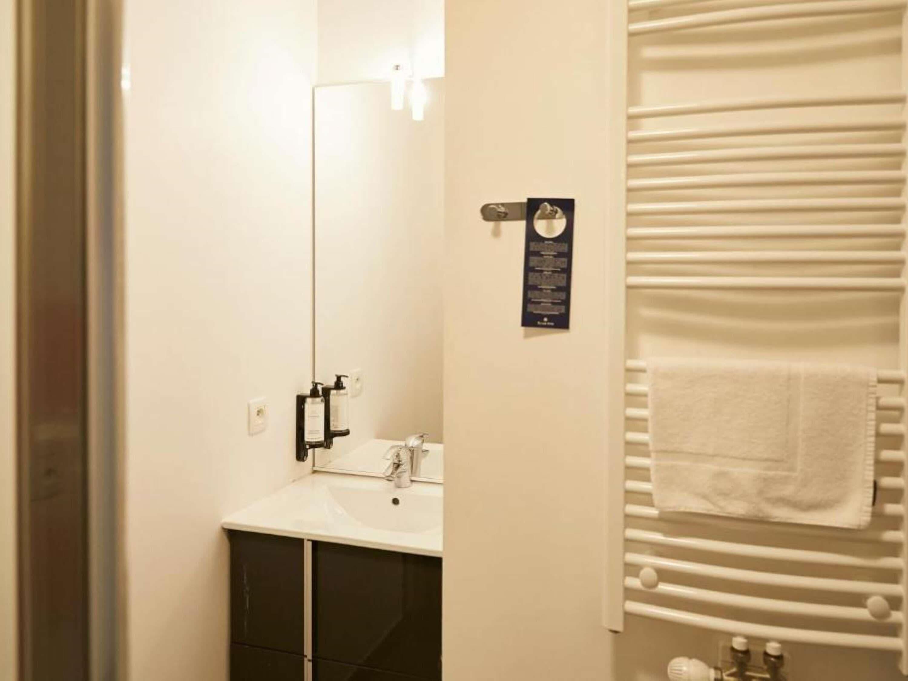 Un baño con espejo, lavabo, toallero y un cartel en la pared.