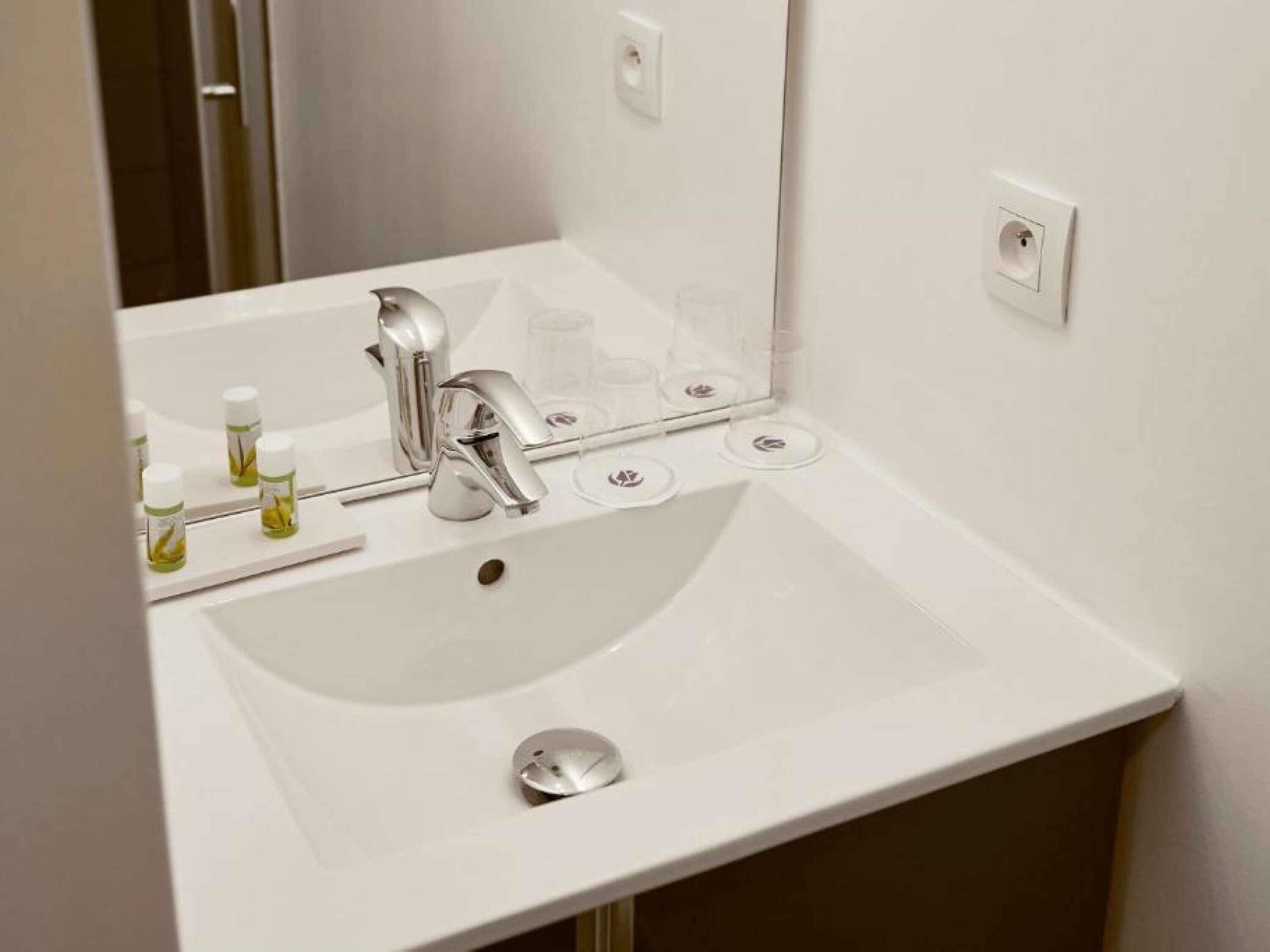 Un lavabo bianco con un rubinetto moderno, uno specchio e alcuni articoli da toilette sul piano di lavoro.