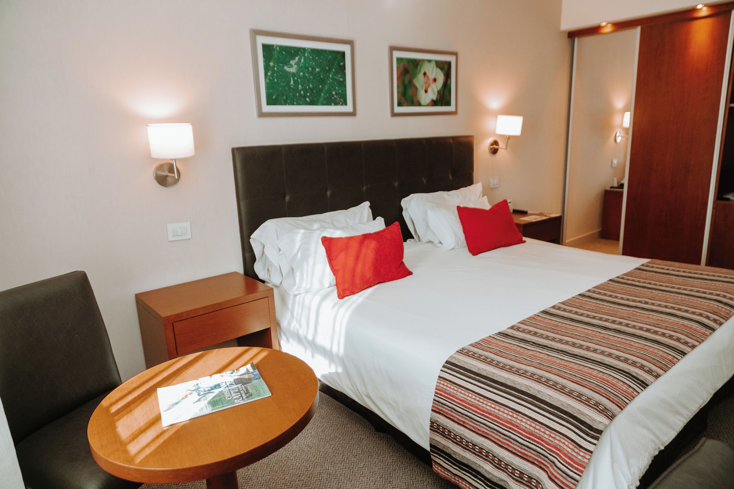 A hotel room with a large bed, two pillows, a nightstand, a round table, and two wall-mounted lamps.