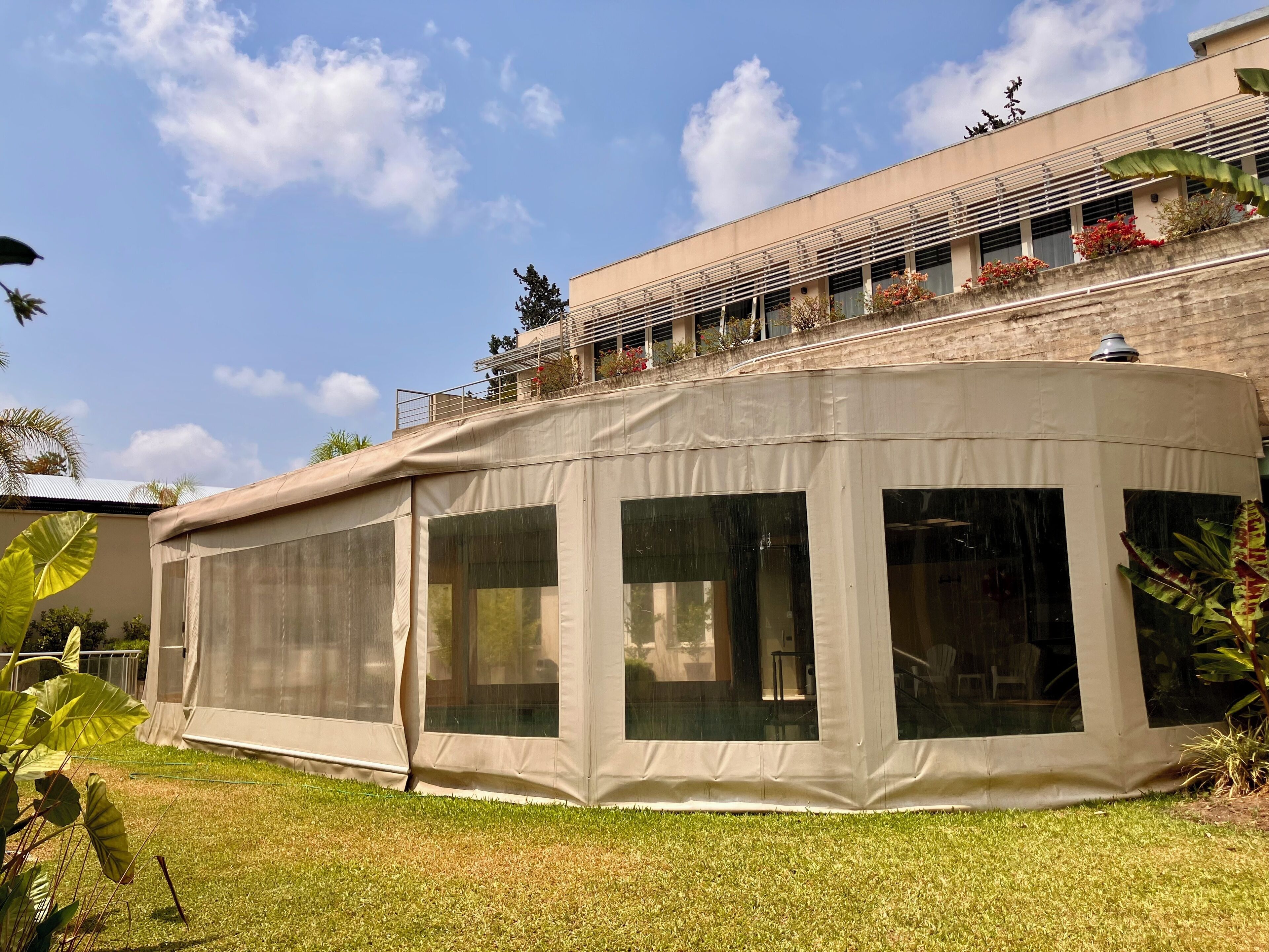 A large, semi-open structure with multiple windows, likely a covered outdoor area or lounge, adjacent to a building with a balcony.