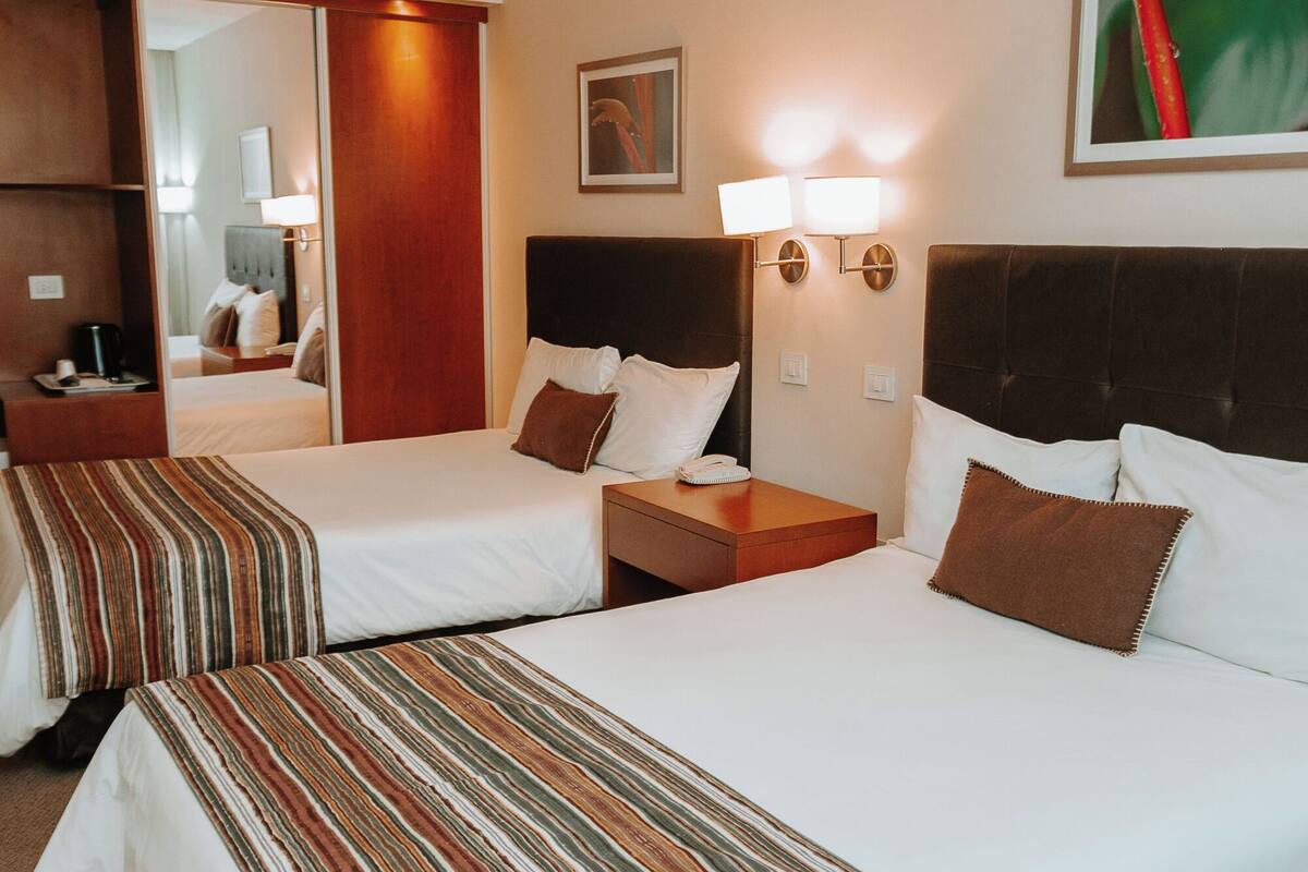 Une chambre d’hôtel avec deux lits, un grand miroir, une table de chevet avec une lampe et un tableau au mur.