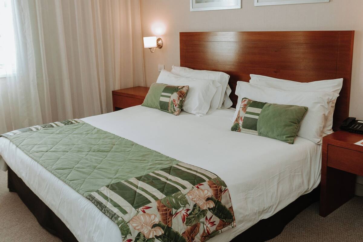 Habitación de hotel con una cama grande, una mesita de noche, una lámpara y dos cuadros en la pared.