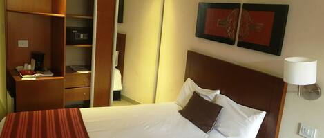 A hotel room with a bed, a bedside table with a phone, a mirror, a wardrobe, and two framed pictures on the wall.