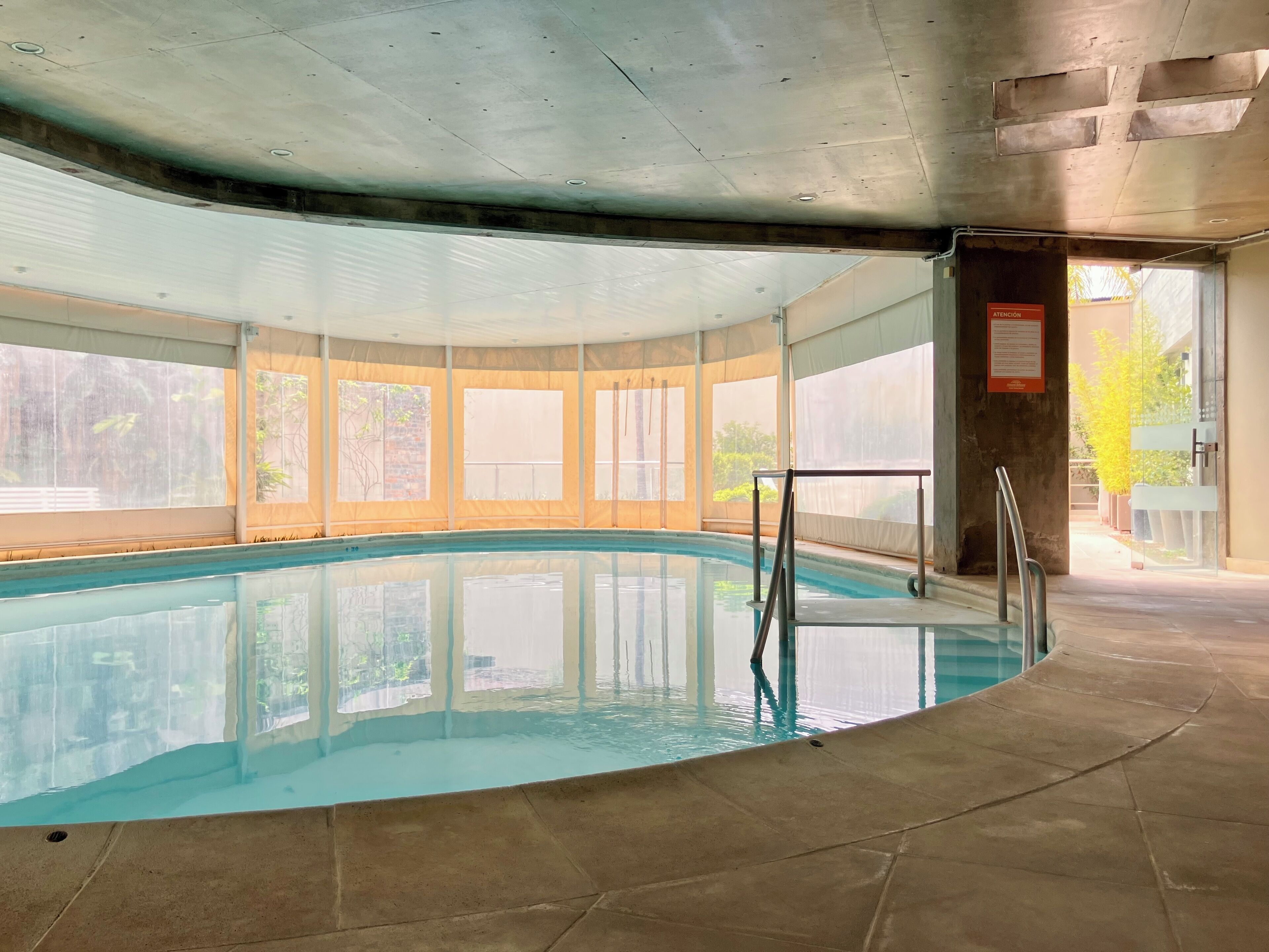 Une piscine intérieure avec des parois en verre transparent, un sol carrelé et un escalier en métal.