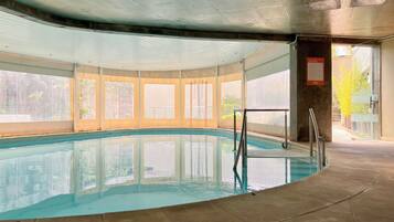 Une piscine intérieure avec des parois en verre transparent, un sol carrelé et un escalier en métal.