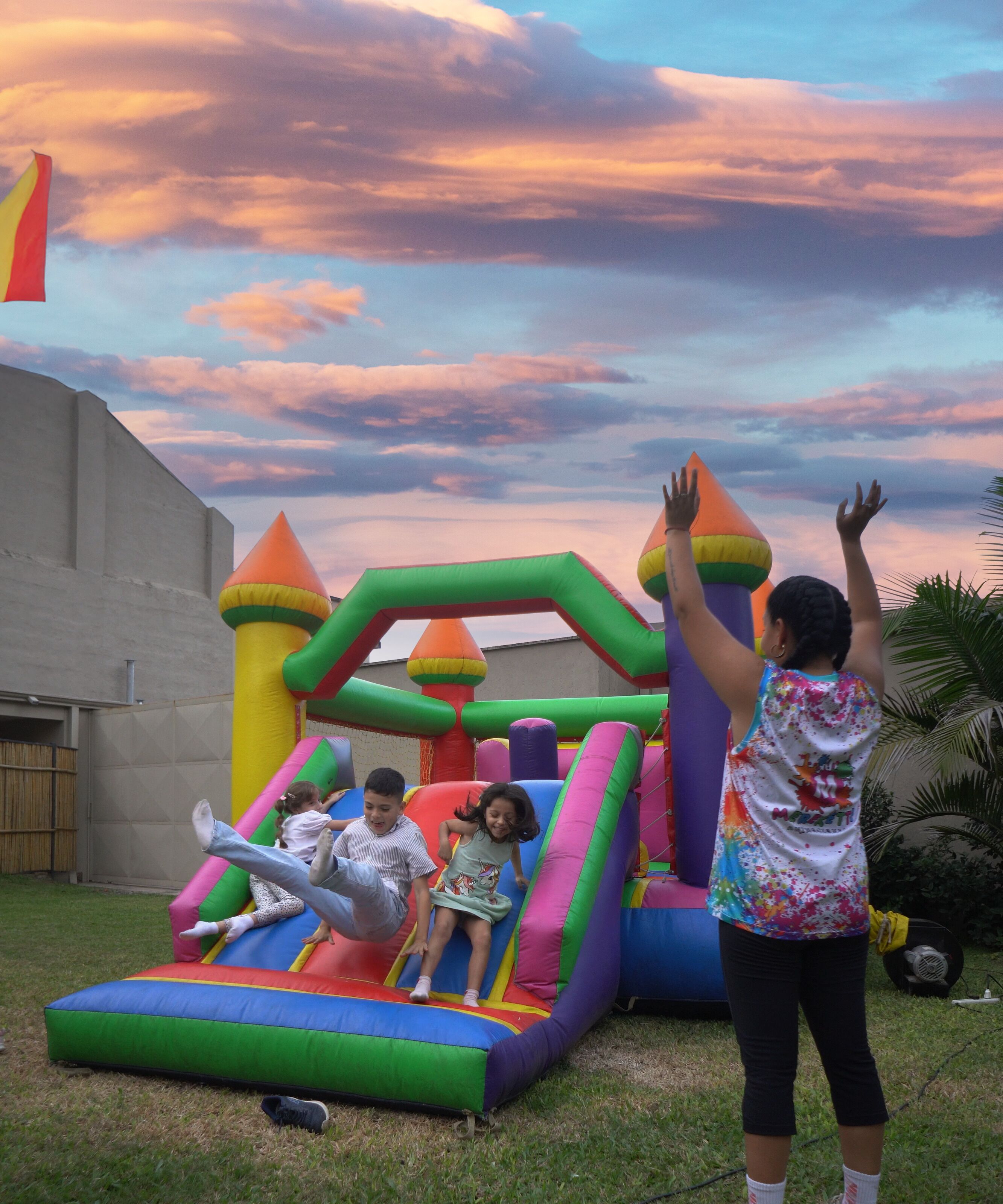Eine farbenfrohe, aufblasbare Spielkonstruktion in einem Garten mit Sonnenuntergang am Himmel.