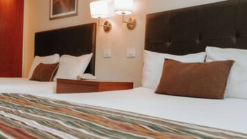 Habitación de hotel con una cama grande, dos mesitas de noche, un cabecero y dos lámparas fijadas a la pared.