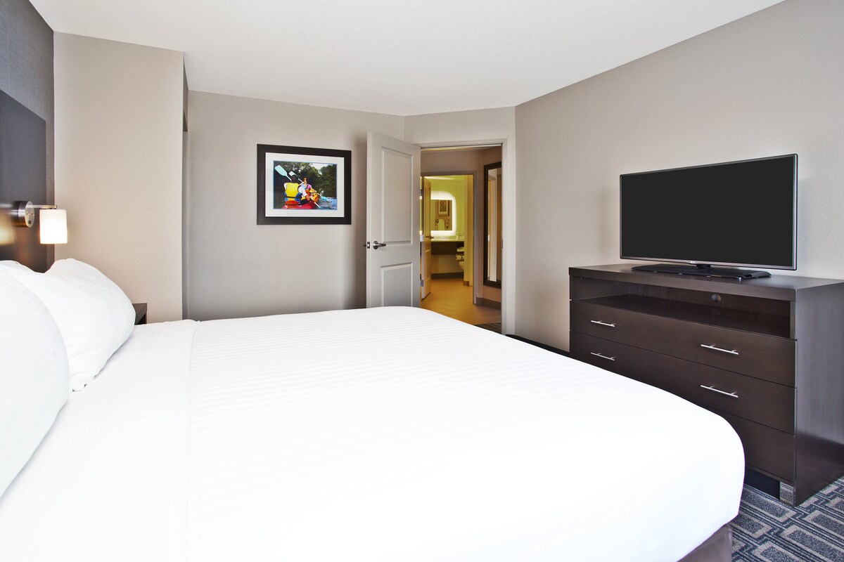 A hotel room with a large bed, a flat-screen TV on a dresser, and a framed picture on the wall.