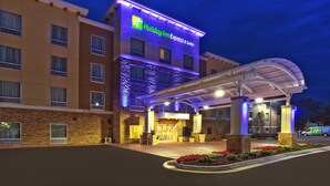 Edificio de Holiday Inn Express & Suites con fachada de ladrillo, entrada cubierta y área de estacionamiento con una camioneta al frente.