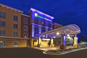 Edificio de Holiday Inn Express & Suites con fachada de ladrillo, entrada cubierta y área de estacionamiento con una camioneta al frente.