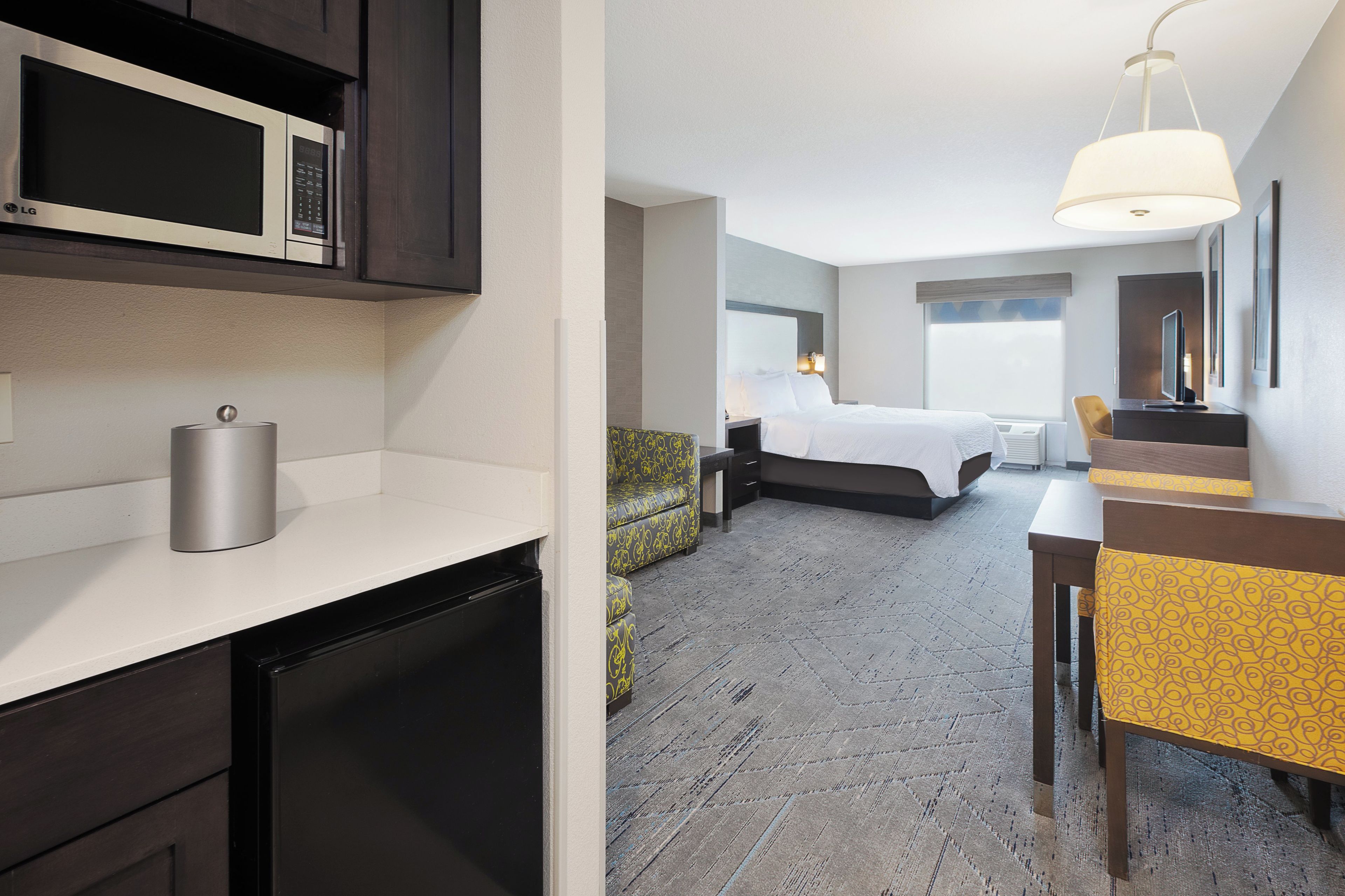 A hotel room with a bed, a desk, a chair, a microwave, and a refrigerator.