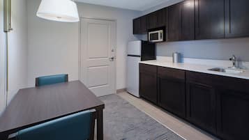 A compact kitchen with dark cabinets, a microwave, a refrigerator, and a dining area with a table and chairs.