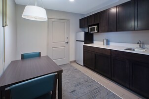 Cocina compacta con armarios oscuros, microondas, refrigerador y comedor con mesa y sillas.