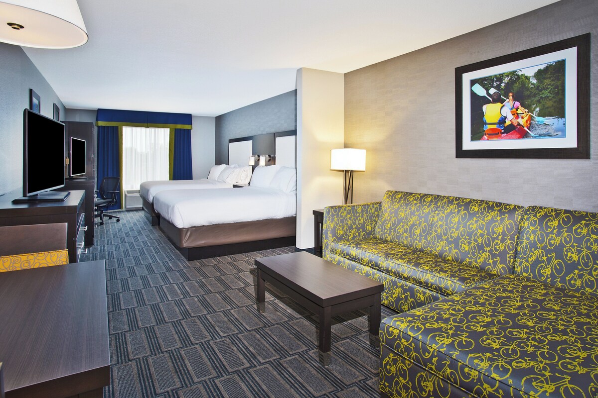 A hotel room with a bed, a sofa, a desk with a TV, and a framed picture on the wall.