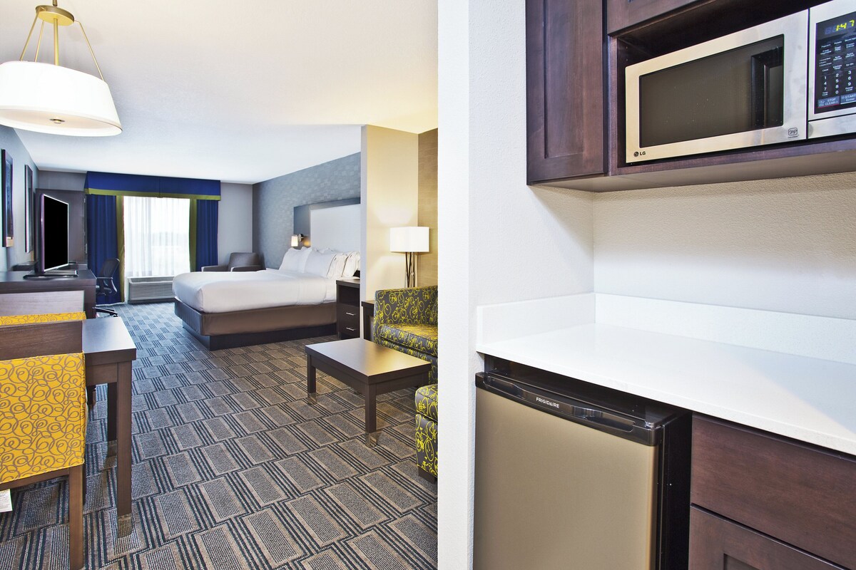 A hotel room with a bed, desk, chair, and a microwave above the counter.