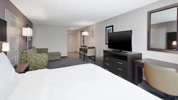 A hotel room with a bed, a desk, a television, and seating area.