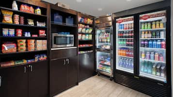 Un espacio de comida autoservicio con dispensadores de bebidas refrigeradas y un microondas.