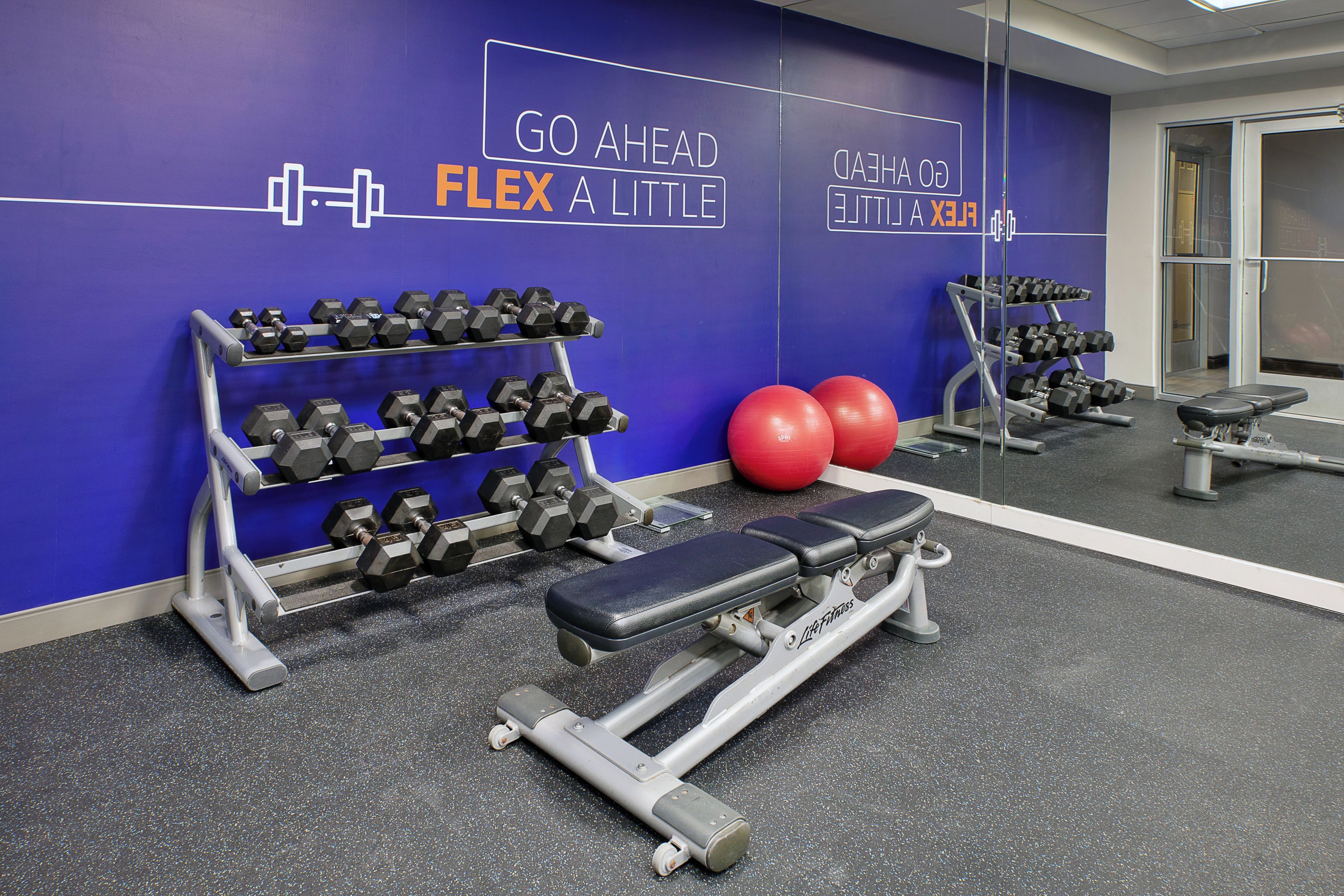 A gym with exercise equipment, a bench, and motivational wall text.