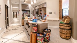 Un vestíbulo de hotel con un mostrador de recepción, un refrigerador de bebidas 'Chilled', una sección 'Frozen' y un letrero que dice 'The Shop'.