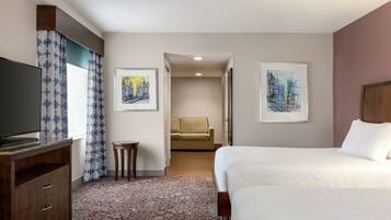 Una habitación de hotel con una cama, televisión, una mesita y dos cuadros en la pared.