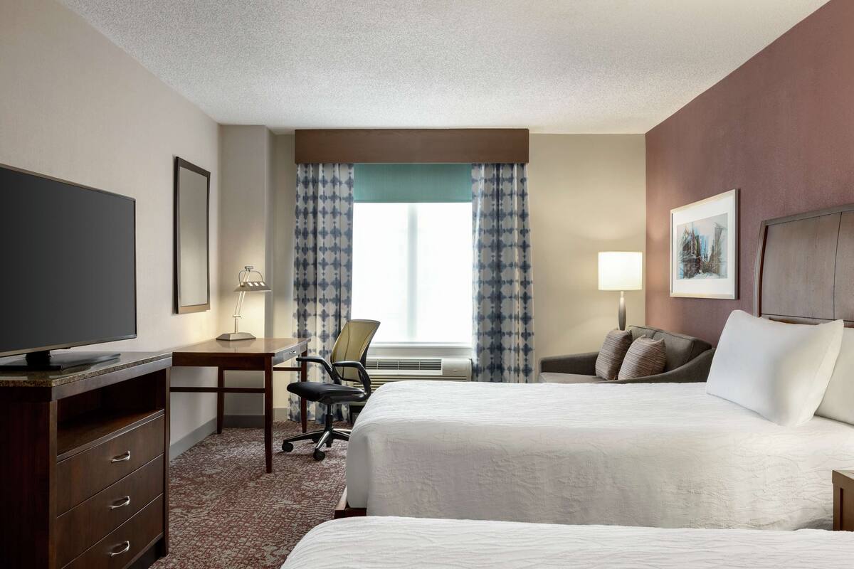A hotel room with a large bed, a desk with a chair, a television, and a window with curtains.