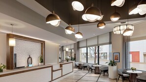 Un área de recepción moderna con una pared texturizada, una mesa de recepción, varias zonas de estar e iluminación colgante.