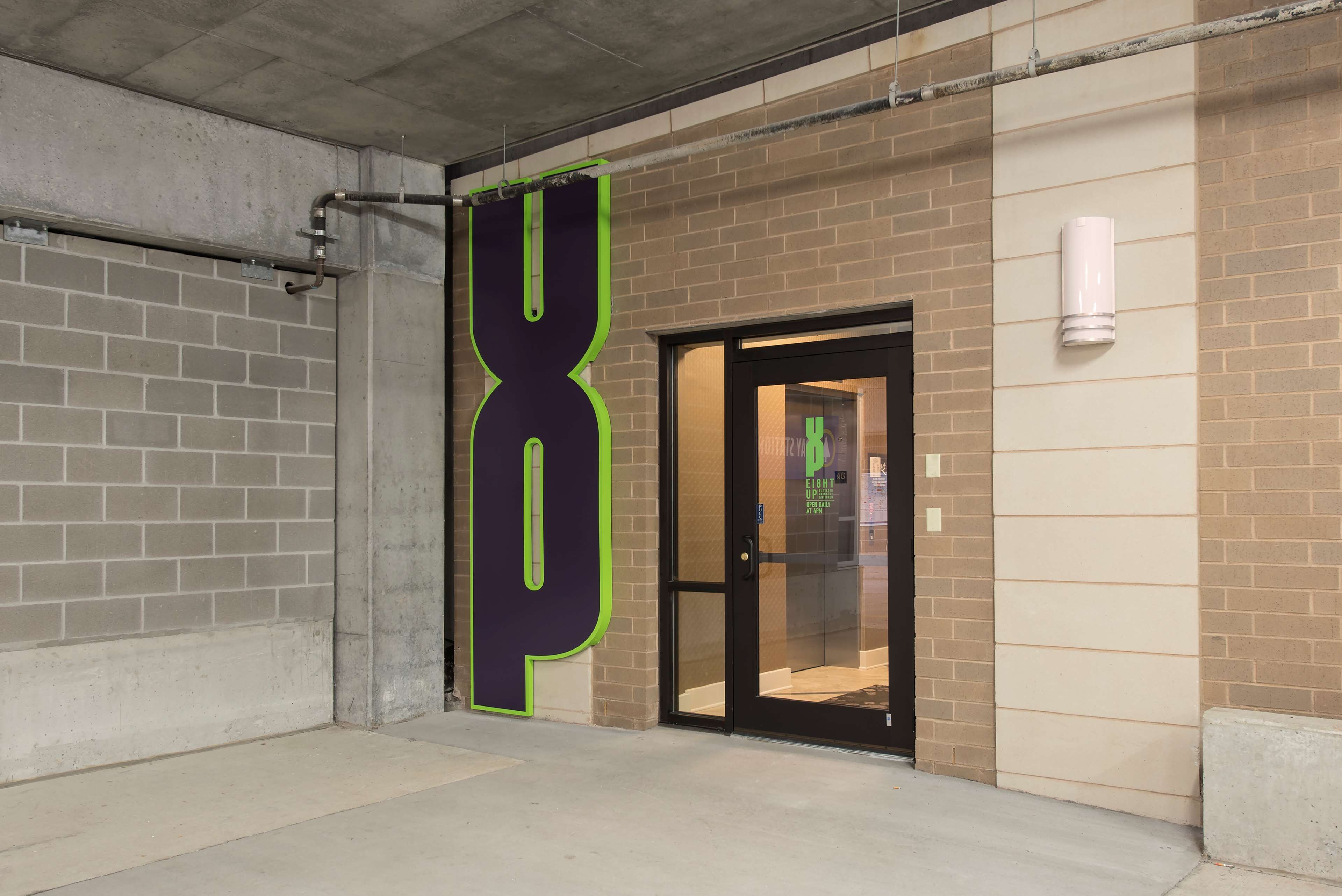 Une entrée d’immeuble avec un grand panneau portant le chiffre « 8 », une porte en verre et un mur en briques.
