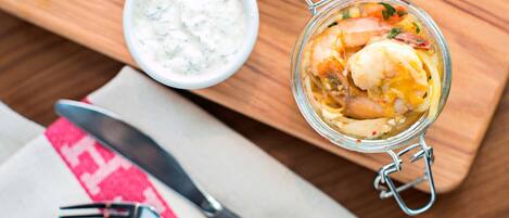 Un tarro de vidrio con cierre metálico que contiene un plato de mariscos, un cuenco pequeño de salsa blanca y un cuchillo y tenedor sobre una mesa de madera.