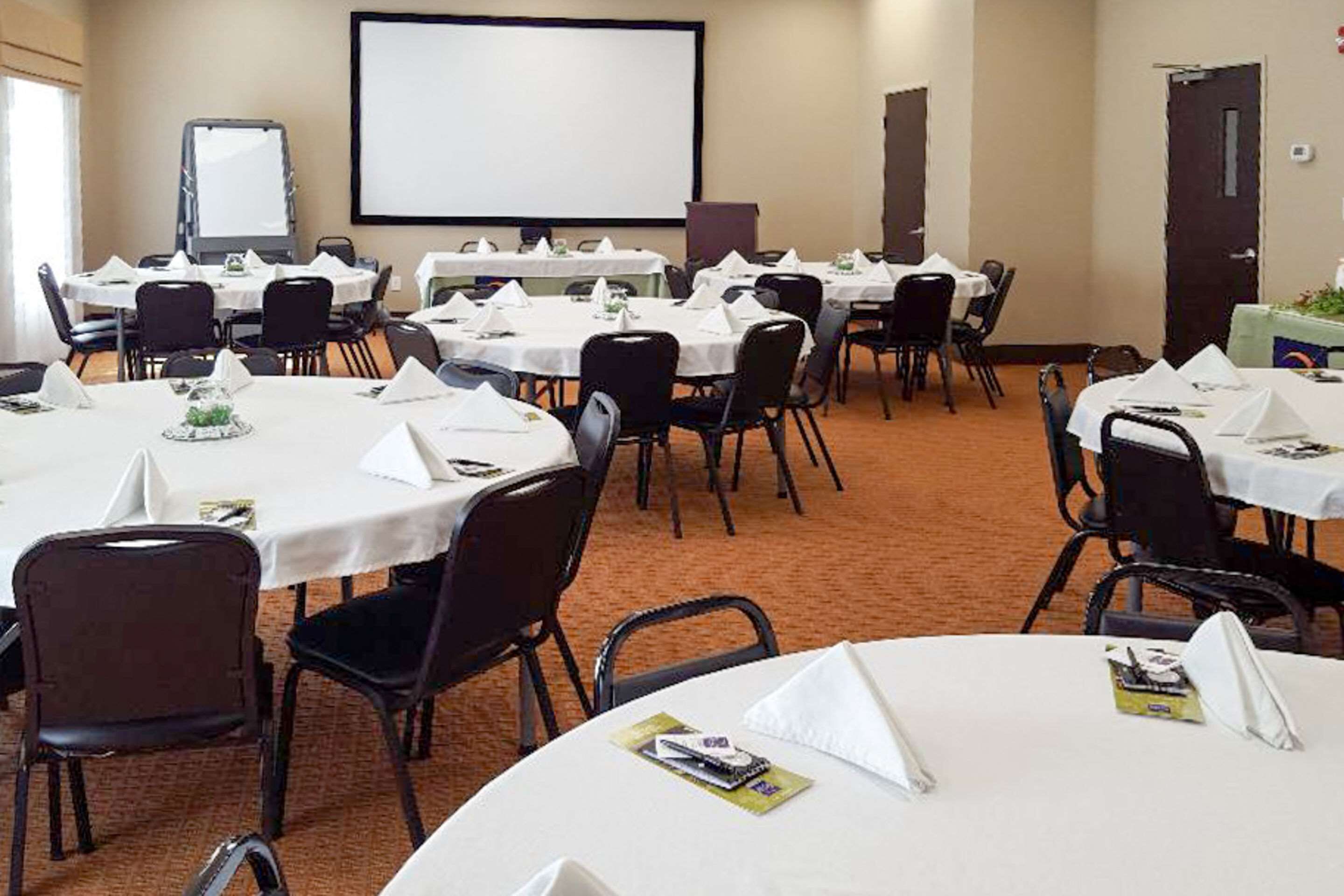 A conference room with multiple tables, chairs, a projector screen, and a whiteboard.