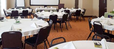 A conference room with multiple tables, chairs, a projector screen, and a whiteboard.