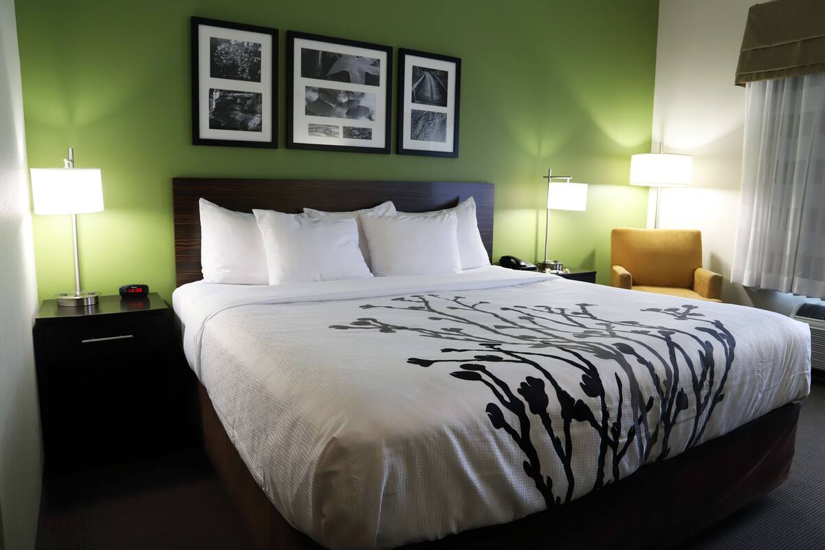 A hotel room with a large bed, two bedside tables, a chair, and a wall with three framed pictures.